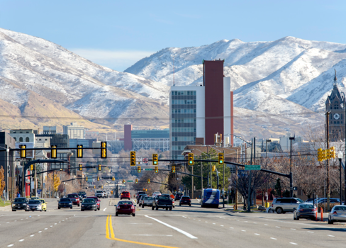 A city street with a tall building and snowy mountains in the background.