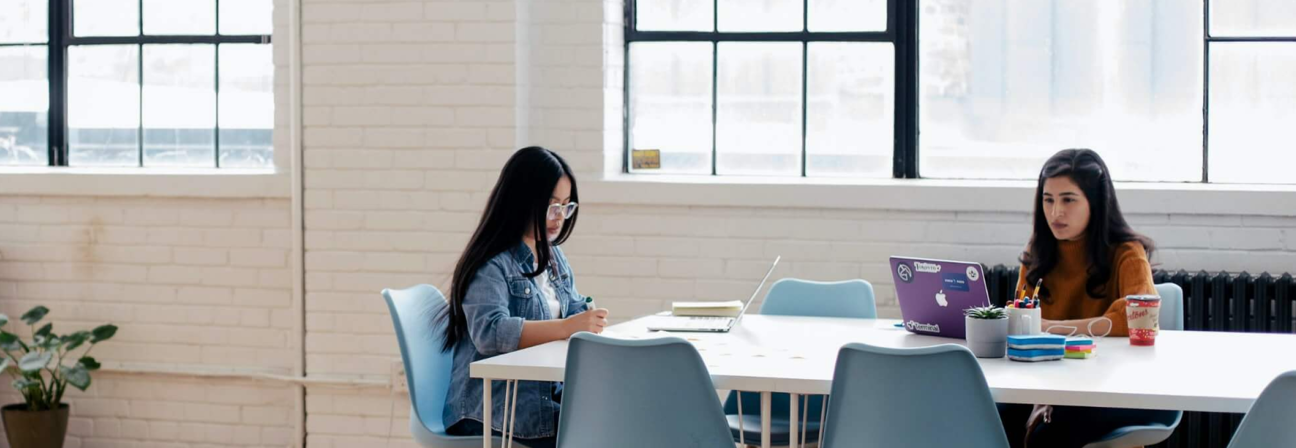 A couple of women sitting at a table with laptops.