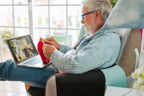 An old man sitting in a chair using a laptop.