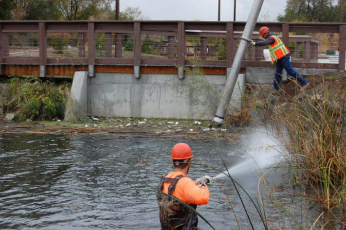 A man on a ladder in a river with a man on a bicycle.