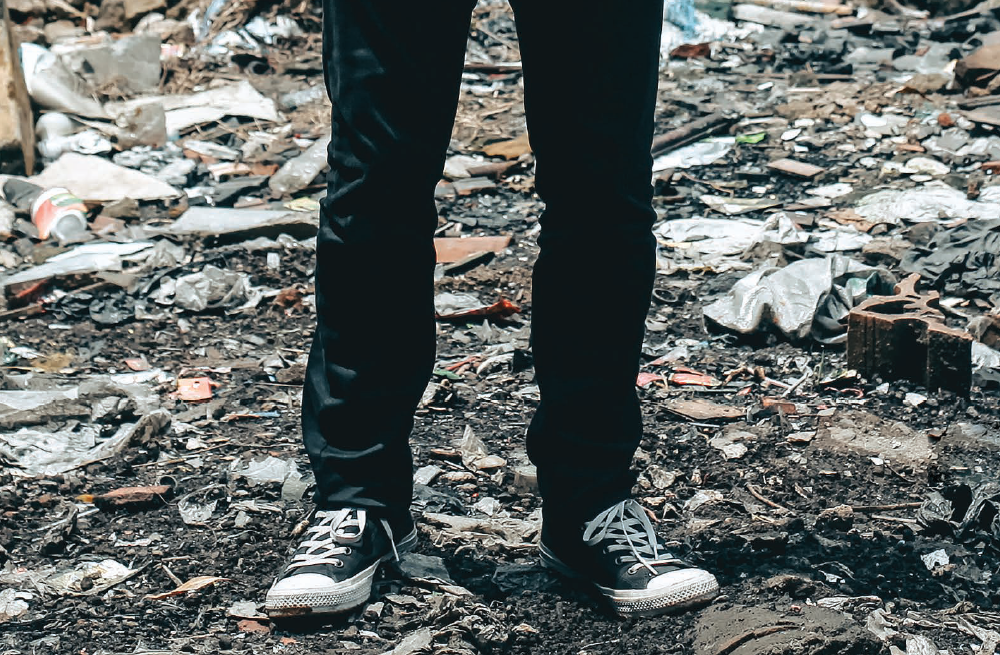 A pair of legs in jeans and shoes standing on a pile of leaves.