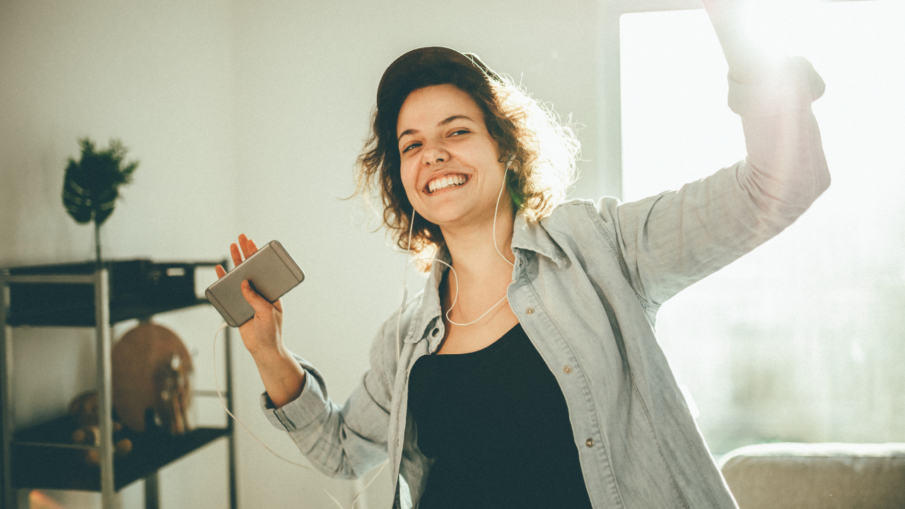 A woman with headphones on holding a phone.