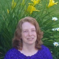 A person smiling in front of a bush of flowers.