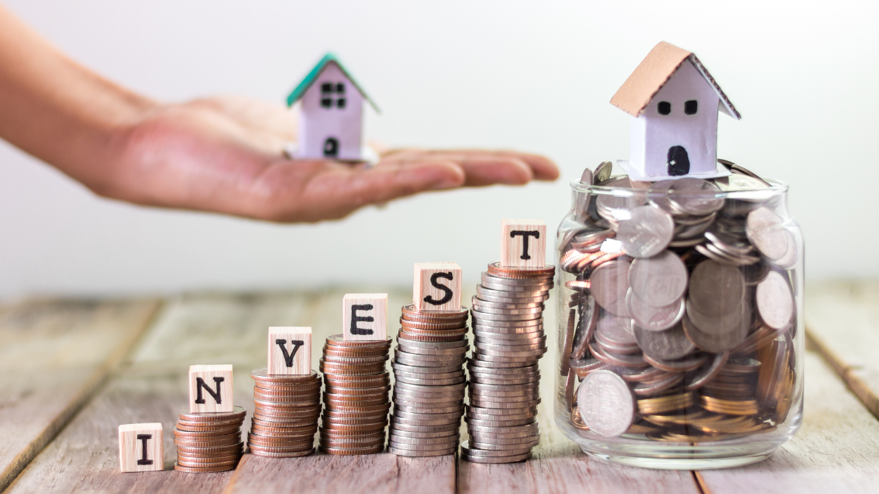 A hand holding a small model of a house and some coins.
