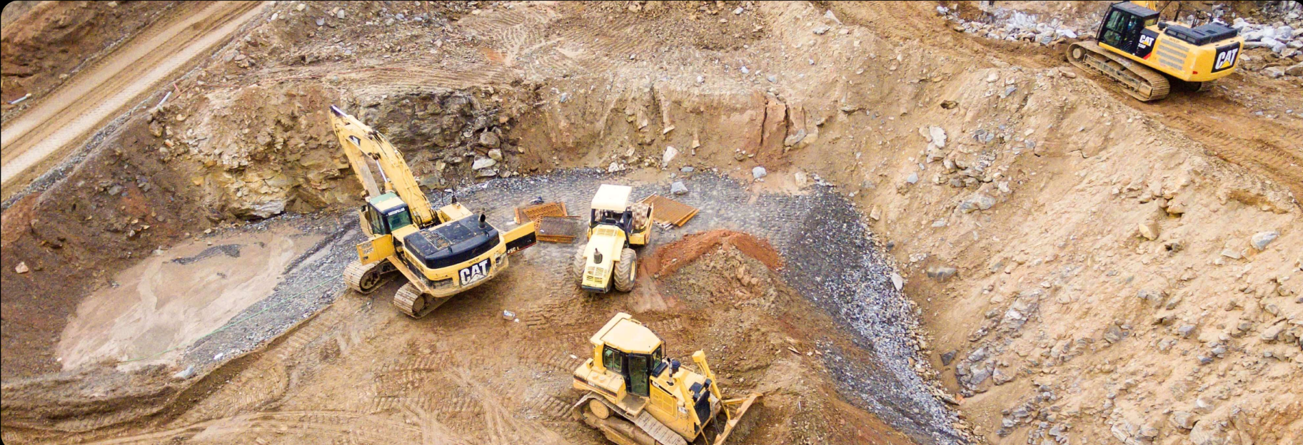 Several yellow construction vehicles in a dirt field.
