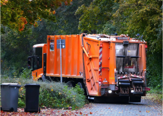 A large orange truck is parked in a wooded area.