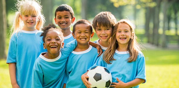 A group of smiling kids in blue shirts with a soccer ball.